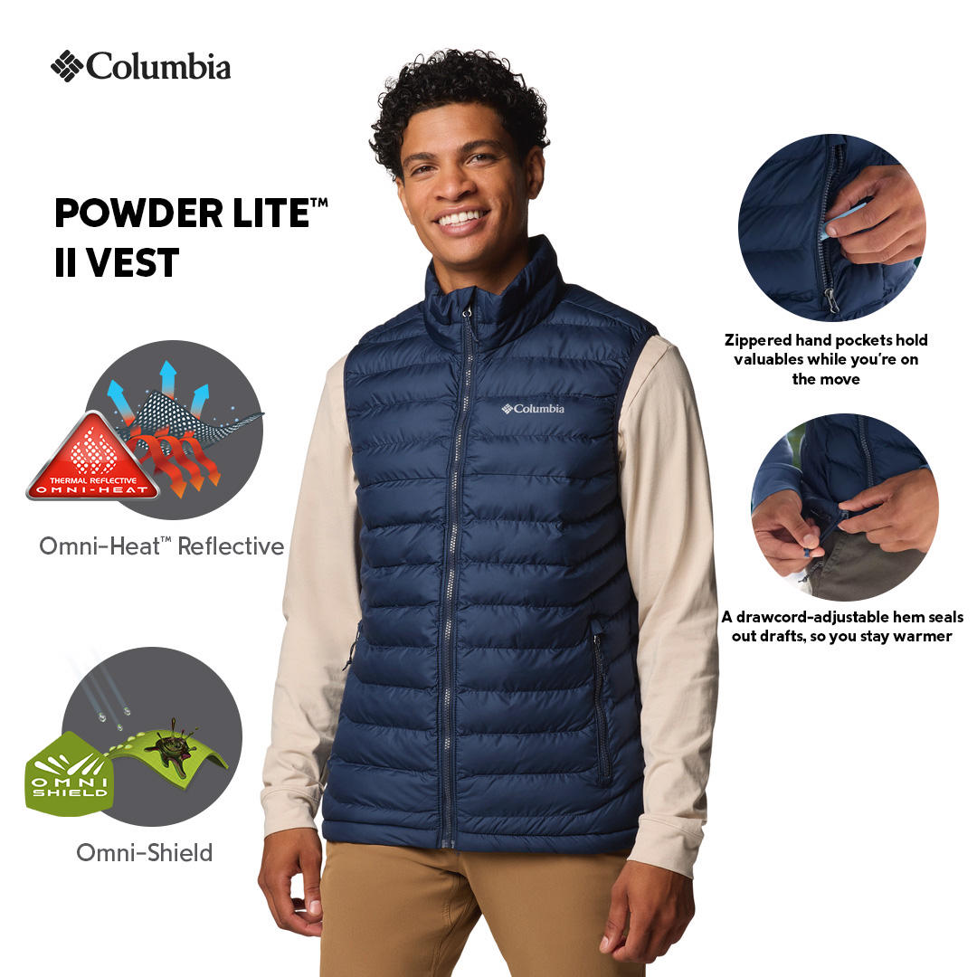 A man wearing a blue quilted vest over a beige long-sleeve shirt and brown pants. The vest has a zipper front and the man has his hands in the zippered hand pockets.